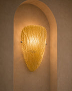 A warm golden textured glass sconce mounted on a beige plaster wall within a recessed archway.