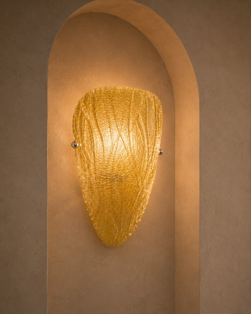 A warm golden textured glass sconce mounted on a beige plaster wall within a recessed archway.