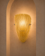 A textured, ribbed glass wall sconce in a warm golden-yellow hue, mounted on a beige plaster wall within a recessed archway.