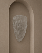 A modern wall sconce with a textured, organic-shaped frosted glass shade and two small silver metal balls on either side, mounted on a warm beige plaster wall with an arched recess.