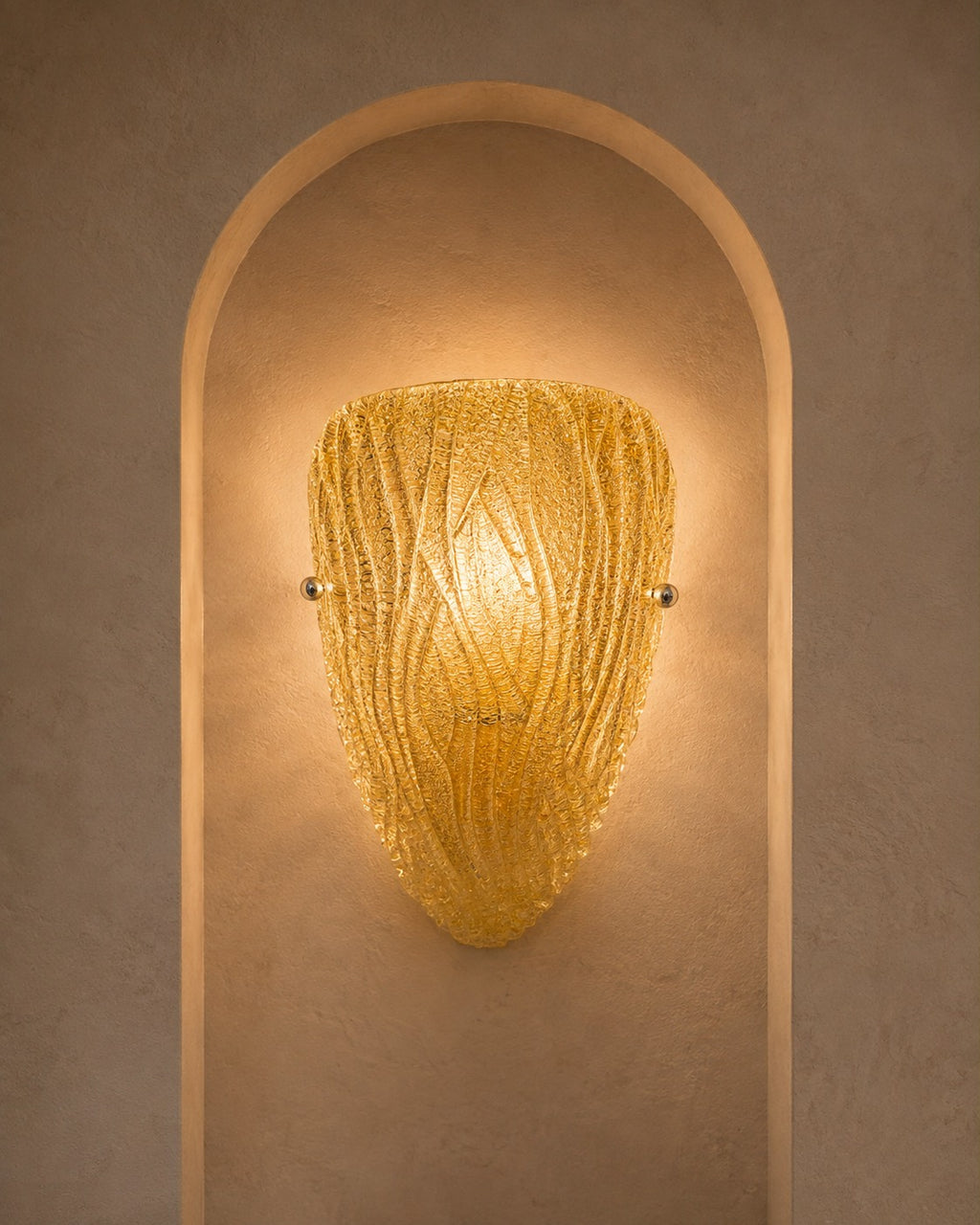 A textured golden-yellow glass sconce with a ribbed, organic shape, mounted on a warm beige plaster wall within an arched recess.
