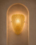 A textured golden-yellow glass sconce with a ribbed, organic shape, mounted on a warm beige plaster wall within an arched recess.