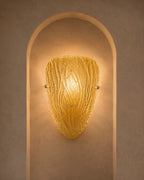 A textured golden-yellow glass sconce with a ribbed, organic shape, mounted on a warm beige plaster wall within an arched recess.
