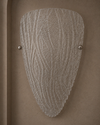 A modern wall sconce light fixture with a textured, organic-shaped clear glass shade and two small metallic silver mounting balls, mounted on a warm brown textured wall.