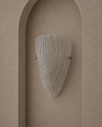 A modern wall sconce with a textured, ribbed clear glass shade and brushed metal hardware, mounted on a warm beige plaster wall with an arched recess.