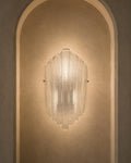 A modern ribbed glass wall sconce mounted on a warm beige plaster wall within an arched niche.