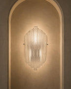 A modern ribbed glass wall sconce mounted on a warm beige plaster wall within an arched niche.