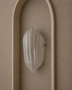 A ribbed clear glass wall sconce mounted on a warm beige plaster wall within an arched recess.