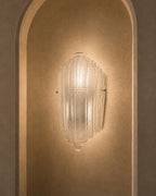 A clear ribbed glass wall sconce mounted on a warm beige plaster wall within an arched niche.