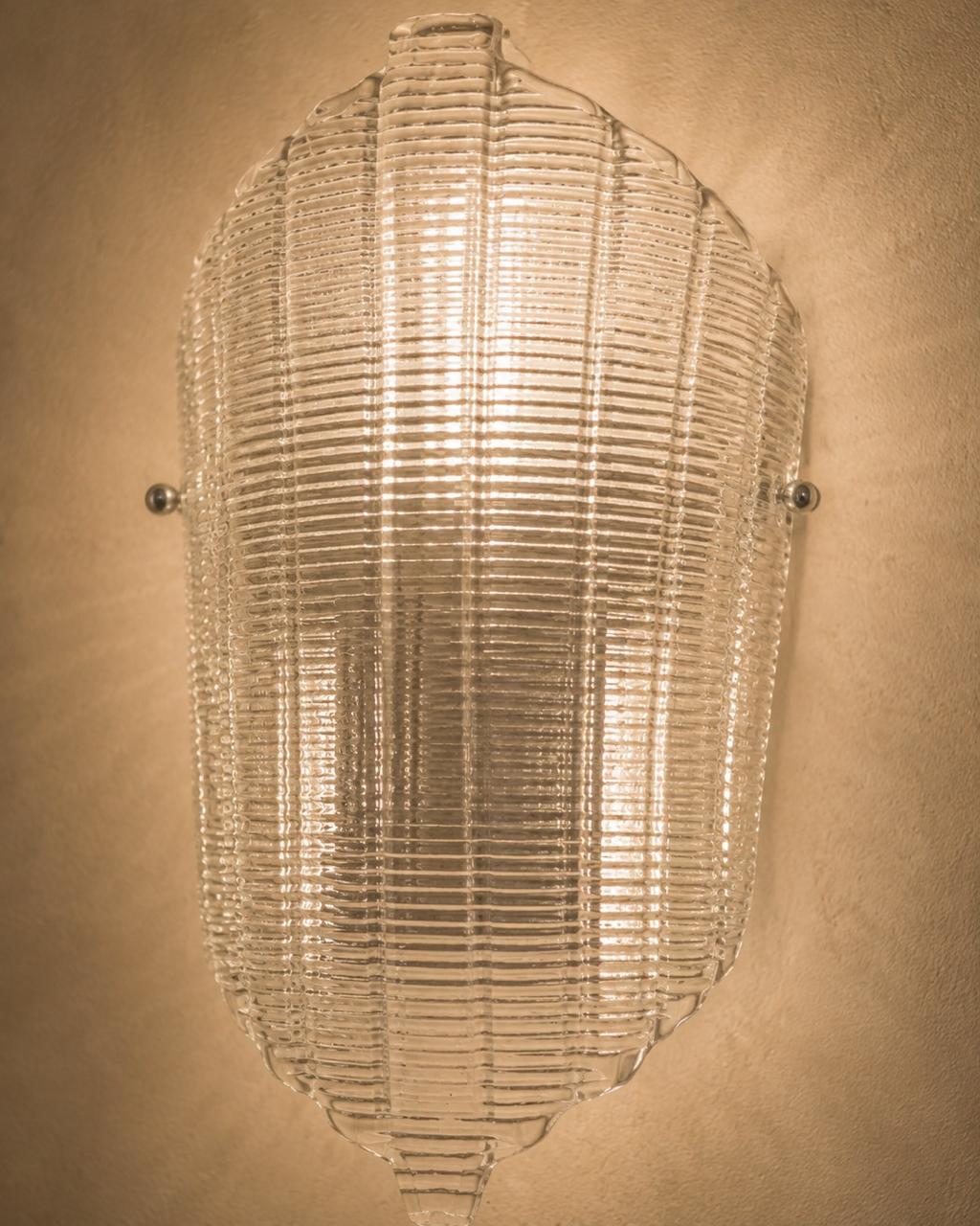 A vintage-style ribbed glass wall sconce with a warm glowing light, mounted on a textured beige wall.