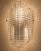 A vintage-style ribbed glass wall sconce with a warm glowing light, mounted on a textured beige wall.