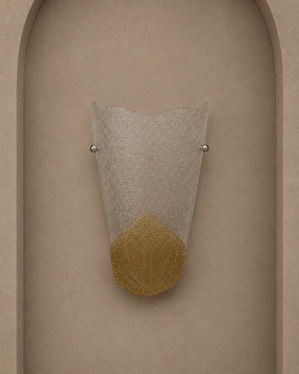 A modern wall sconce with a textured clear glass shade and a gold textured lower section, mounted on a beige stucco wall with an arched recess.