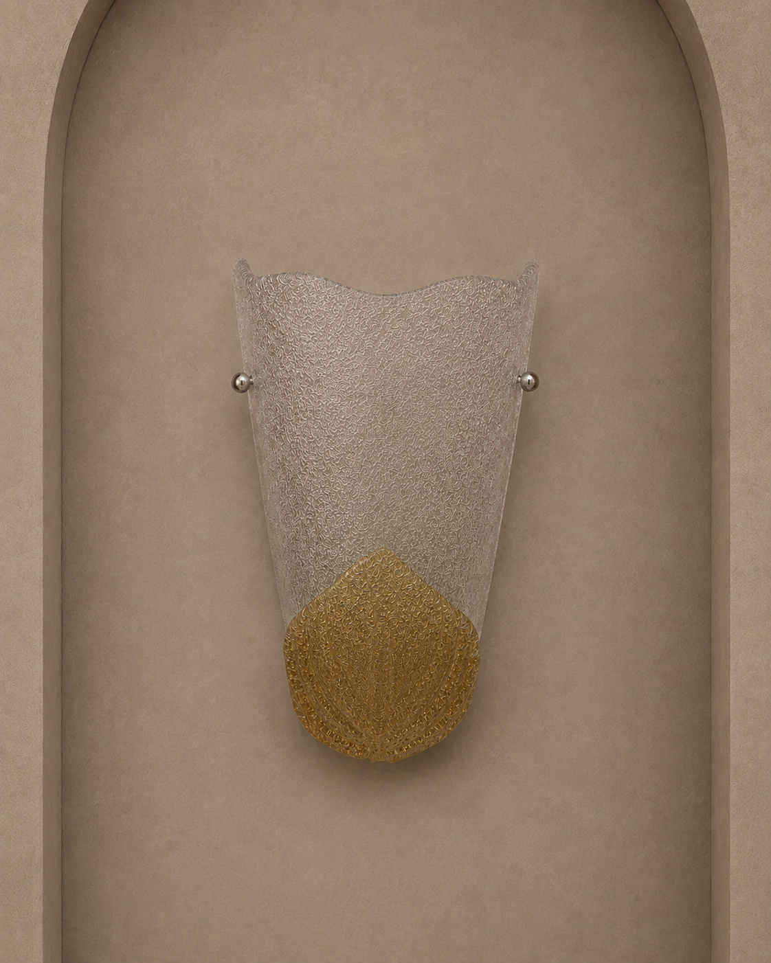A modern wall sconce with a textured clear glass shade and a gold textured lower section, mounted on a beige stucco wall with an arched recess.
