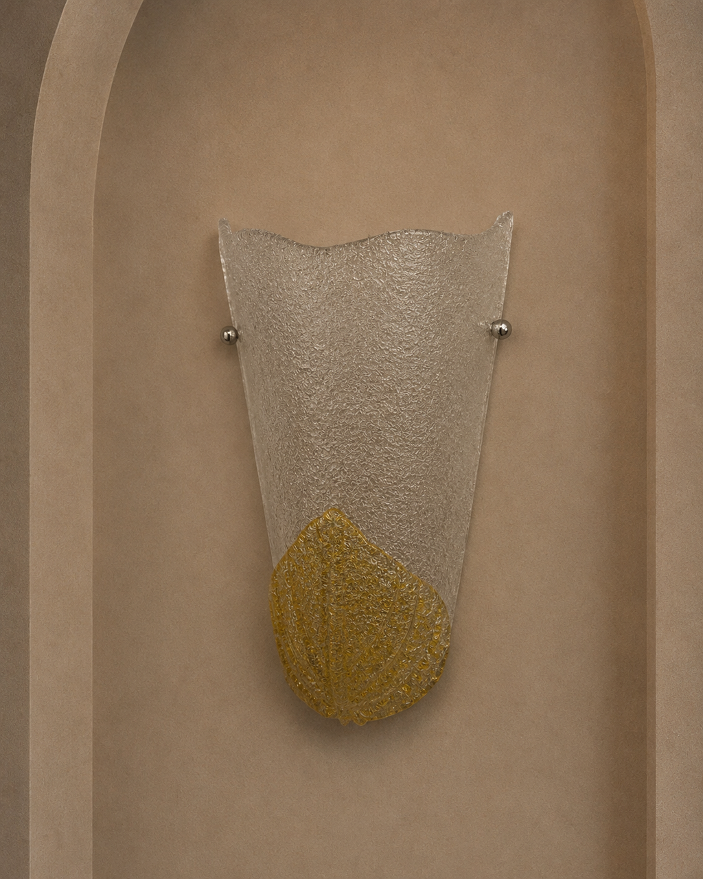 A modern wall sconce light fixture with a textured clear glass shade and a gold leaf-shaped accent at the bottom, mounted on a beige plaster wall in an arched niche.