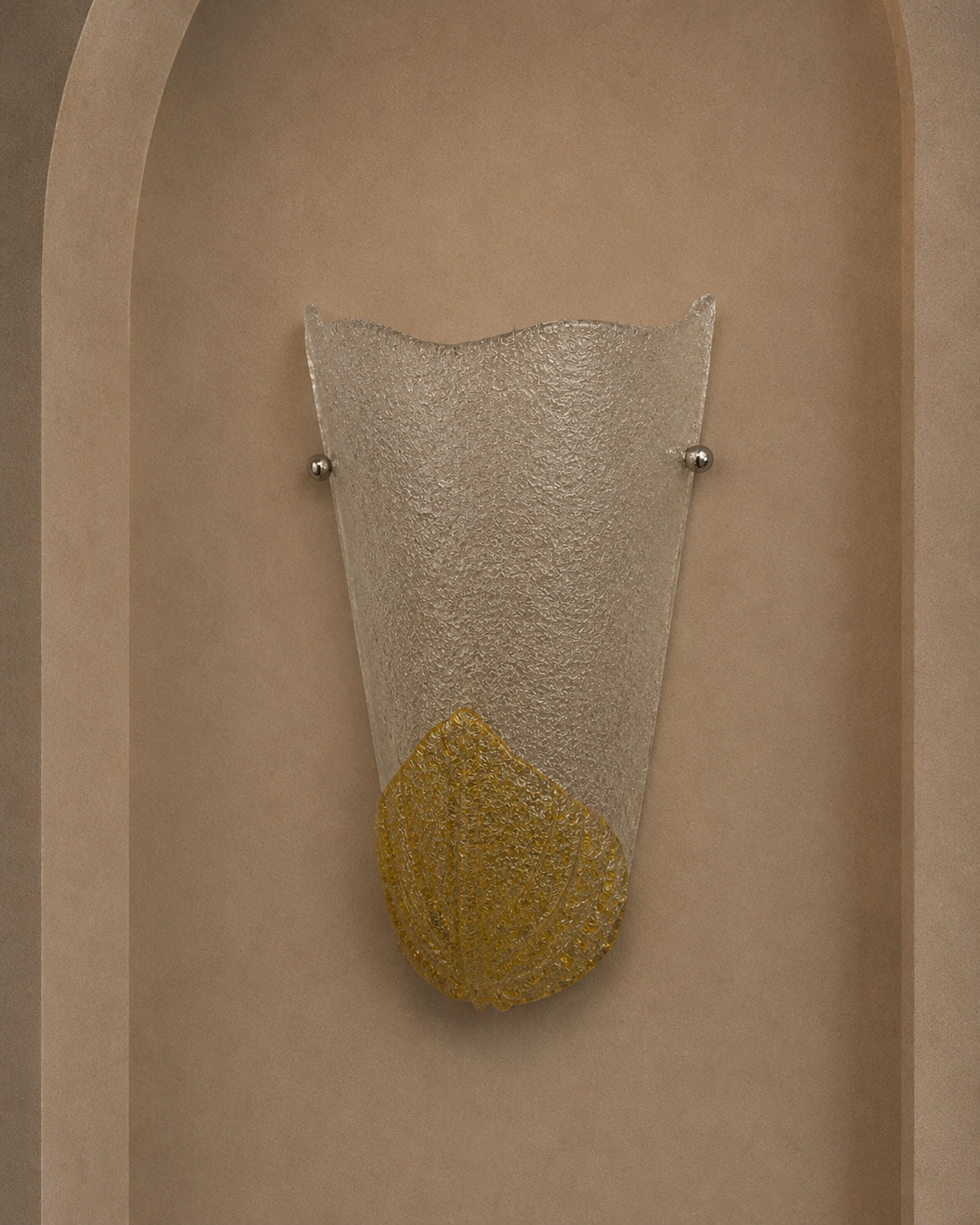 A modern wall sconce light fixture with a textured clear glass shade and a gold leaf-shaped accent at the bottom, mounted on a beige plaster wall in an arched niche.