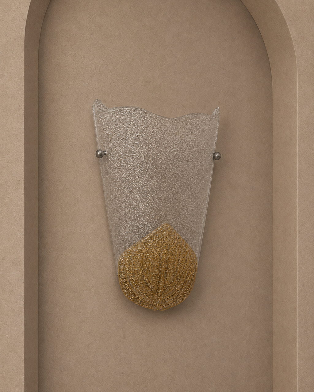 A modern wall sconce with a textured clear glass shade and a gold-colored textured base, mounted on a beige arched wall.