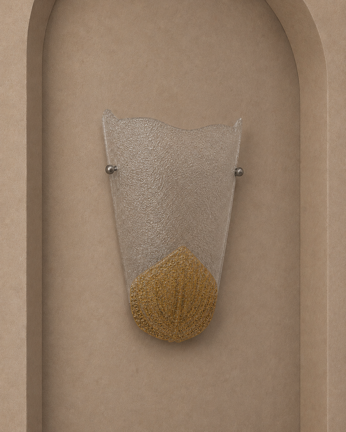 A modern wall sconce with a textured clear glass shade and a gold-colored textured base, mounted on a beige arched wall.