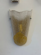 A wall-mounted sconce with a textured, crackled glass shade that transitions from frosted white at the top to metallic gold at the bottom, mounted on a plain white wall.