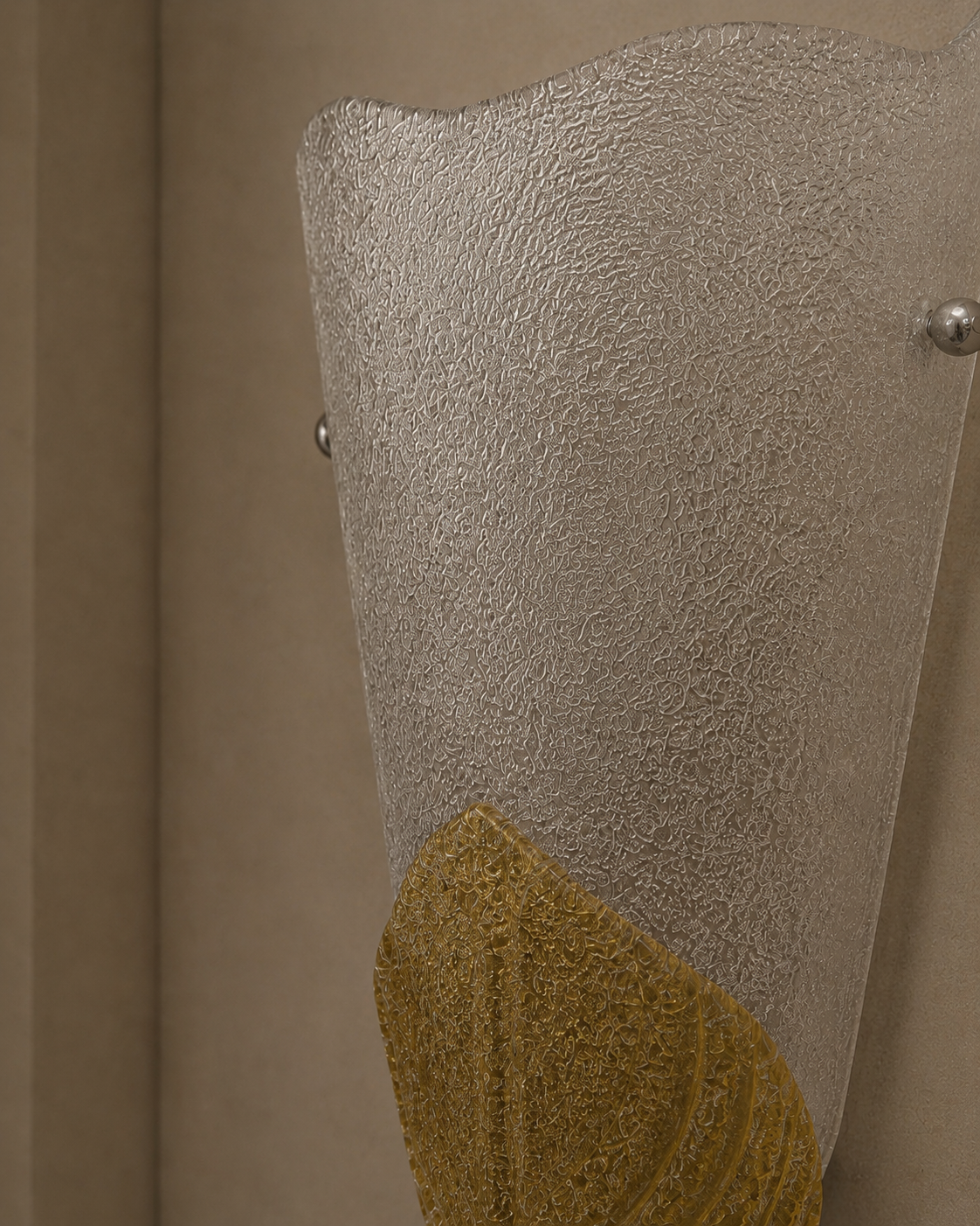 A close-up of a textured glass wall sconce with a wavy top edge, featuring a frosted clear upper section and a textured gold lower section, mounted on a beige wall.