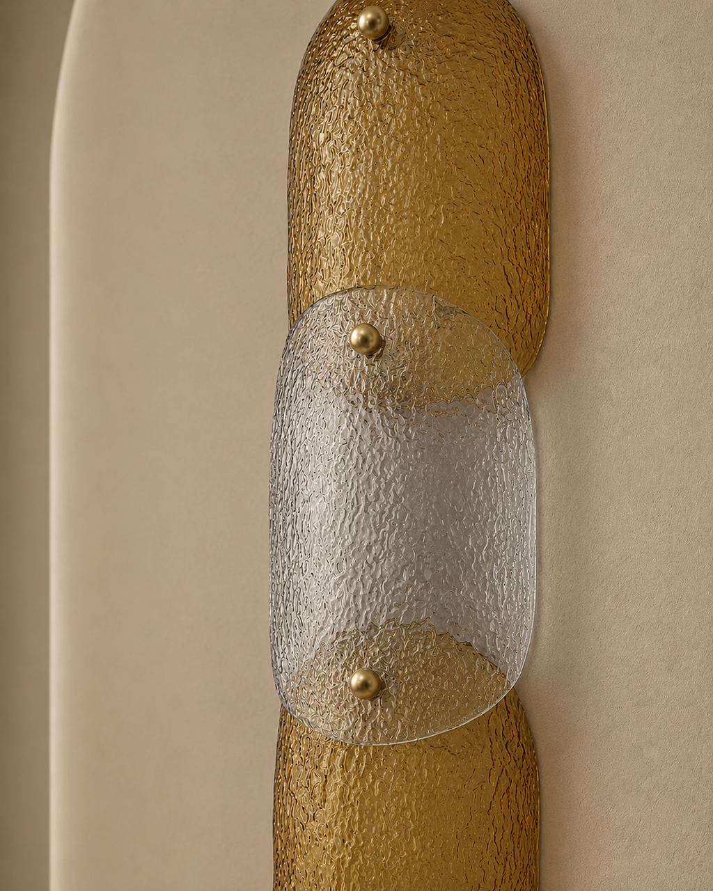 A close-up of a modern wall sconce featuring textured gold glass cylindrical ends and a central clear textured glass panel, mounted on a beige wall.