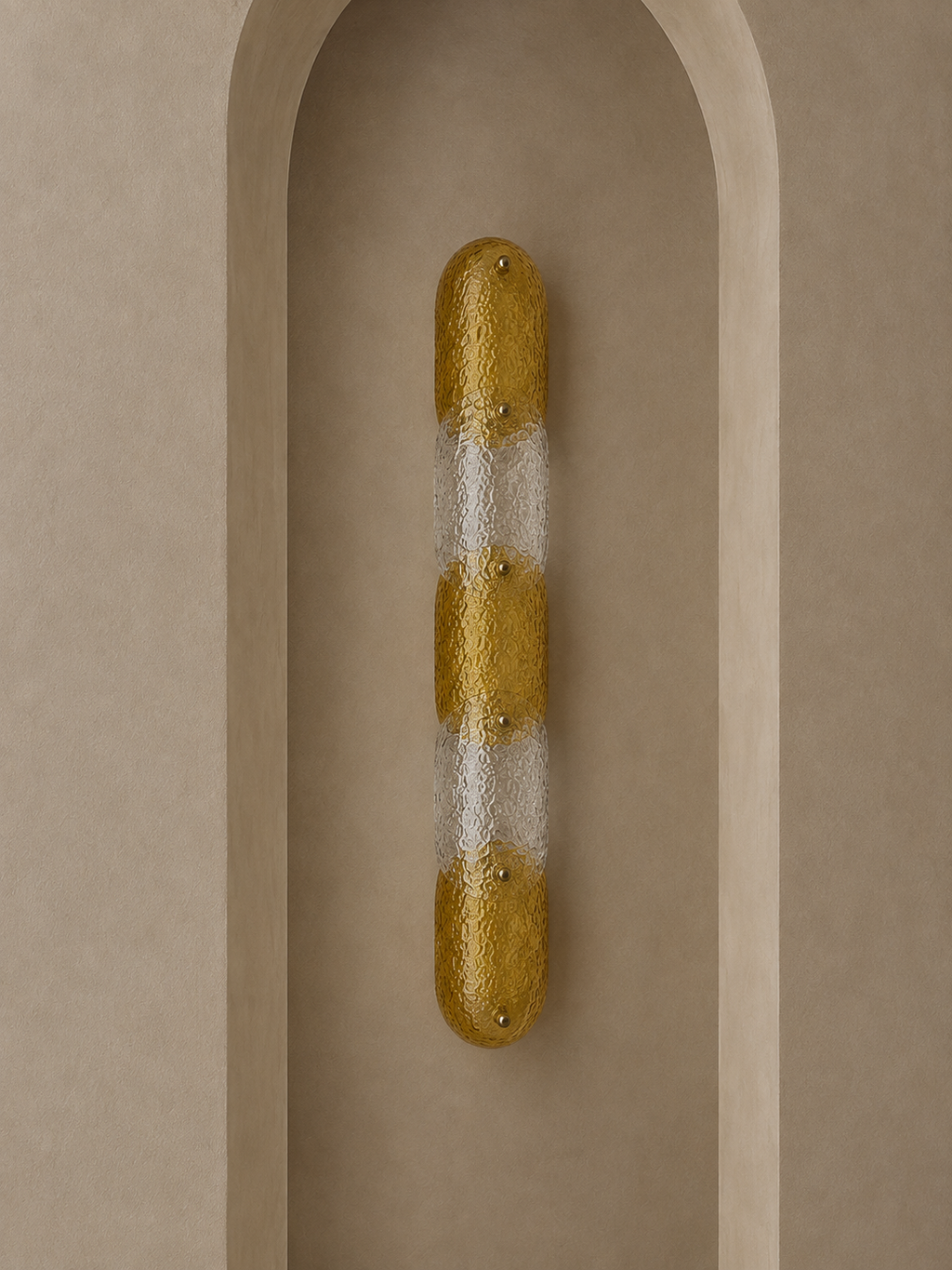 A modern wall sconce with a textured gold and frosted white striped design, mounted on a beige plaster niche.