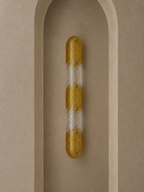 A modern wall sconce with a textured gold and frosted white striped design, mounted on a beige plaster niche.