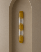 A modern vertical wall sconce with three textured amber-yellow glass segments and two frosted clear glass segments, mounted on a beige arched plaster niche.