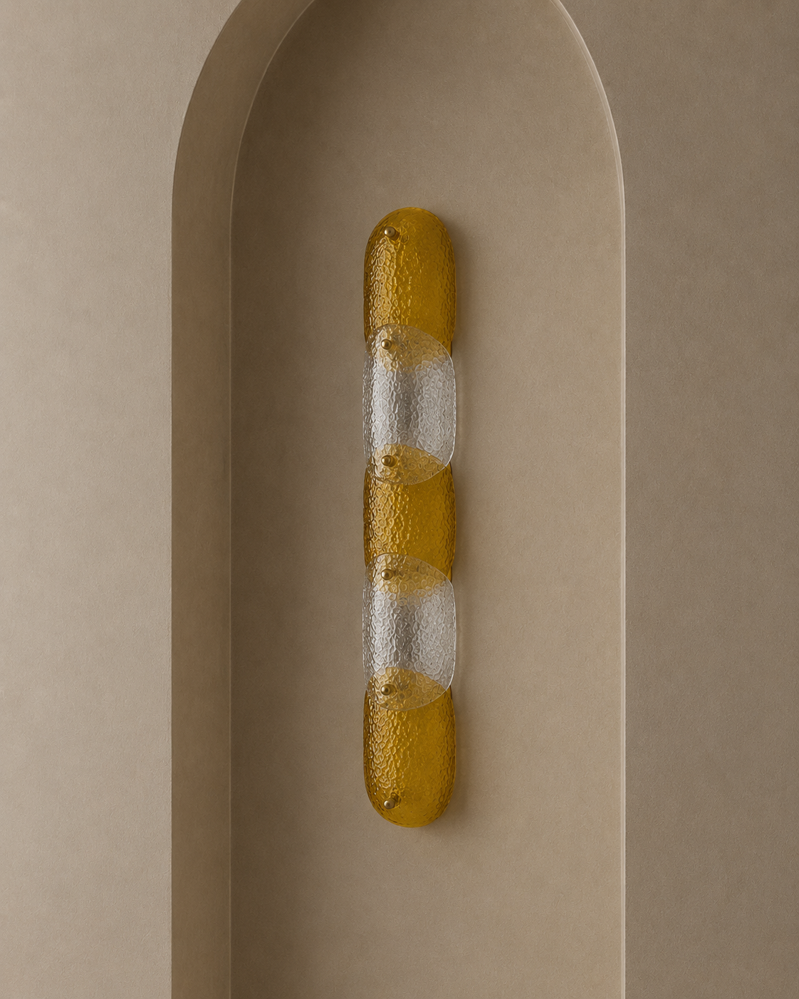 A modern vertical wall sconce with three textured amber-yellow glass segments and two frosted clear glass segments, mounted on a beige arched plaster niche.