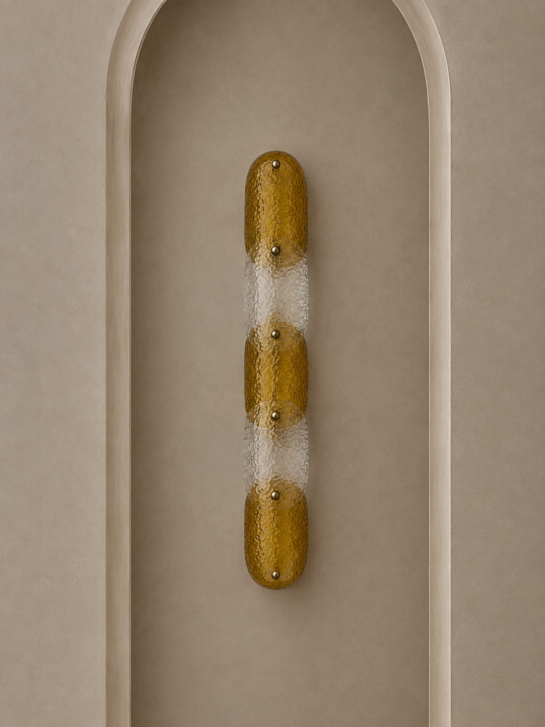 A modern wall sconce with a vertical elongated oval shape, featuring textured metallic gold and frosted white sections, mounted on a beige arched wall.