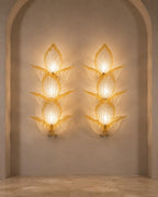 Two matching sculptural wall sconces mounted on a beige plaster wall within an arched alcove. Each sconce has a stacked, lotus-like form made of translucent textured glass or resin, glowing with warm light.