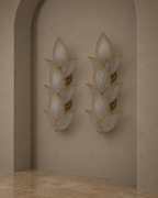 Two matching wall sconces with layered translucent white petal-like shades and gold trim, mounted on a beige plaster wall in an arched alcove with a stone floor.