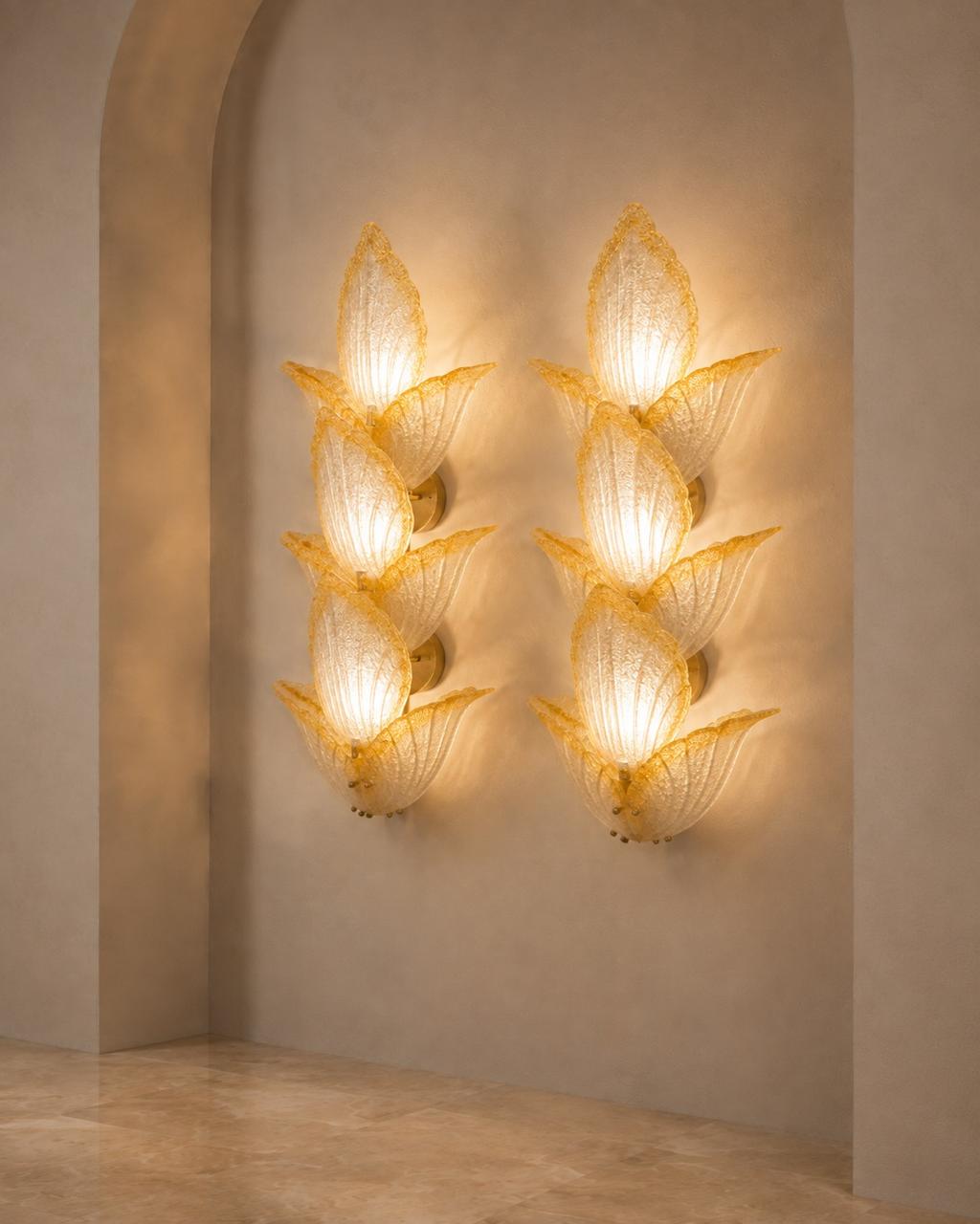 Two matching sculptural wall sconces mounted on a beige plaster wall in an arched alcove. Each sconce has a warm glowing organic, flower-like form made of translucent textured material with a gold-toned base.