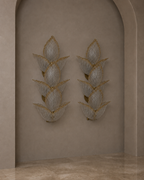Two matching wall sconces with layered leaf-like glass shades and gold-toned metal detailing, mounted on a beige plaster archway in an interior setting.