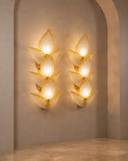 A pair of sculptural wall sconces mounted on a beige plaster wall in an arched alcove. Each sconce features a cluster of translucent, petal-like shades with a warm golden glow emanating from within.