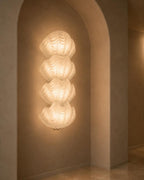 A modern wall-mounted light fixture with three stacked, cloud-like illuminated panels, set into a warm beige plaster archway on a wall.