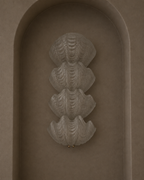 A sculptural wall sconce featuring four stacked, textured clam-shell forms in a warm taupe finish, mounted on a matching arched plaster wall.