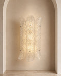 A sculptural wall sconce with a textured, ribbed clear glass shade, mounted on a warm beige plaster wall within an arched niche.