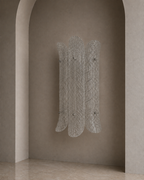 A sculptural wall-mounted coat rack with five vertical textured panels, shown hanging on a warm beige plaster wall in an arched interior setting.