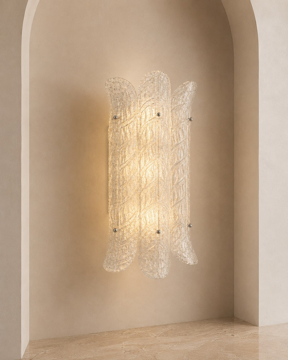 A modern wall sconce with a textured, translucent glass shade featuring a spiral pattern, mounted on a warm beige plaster wall in an arched niche.