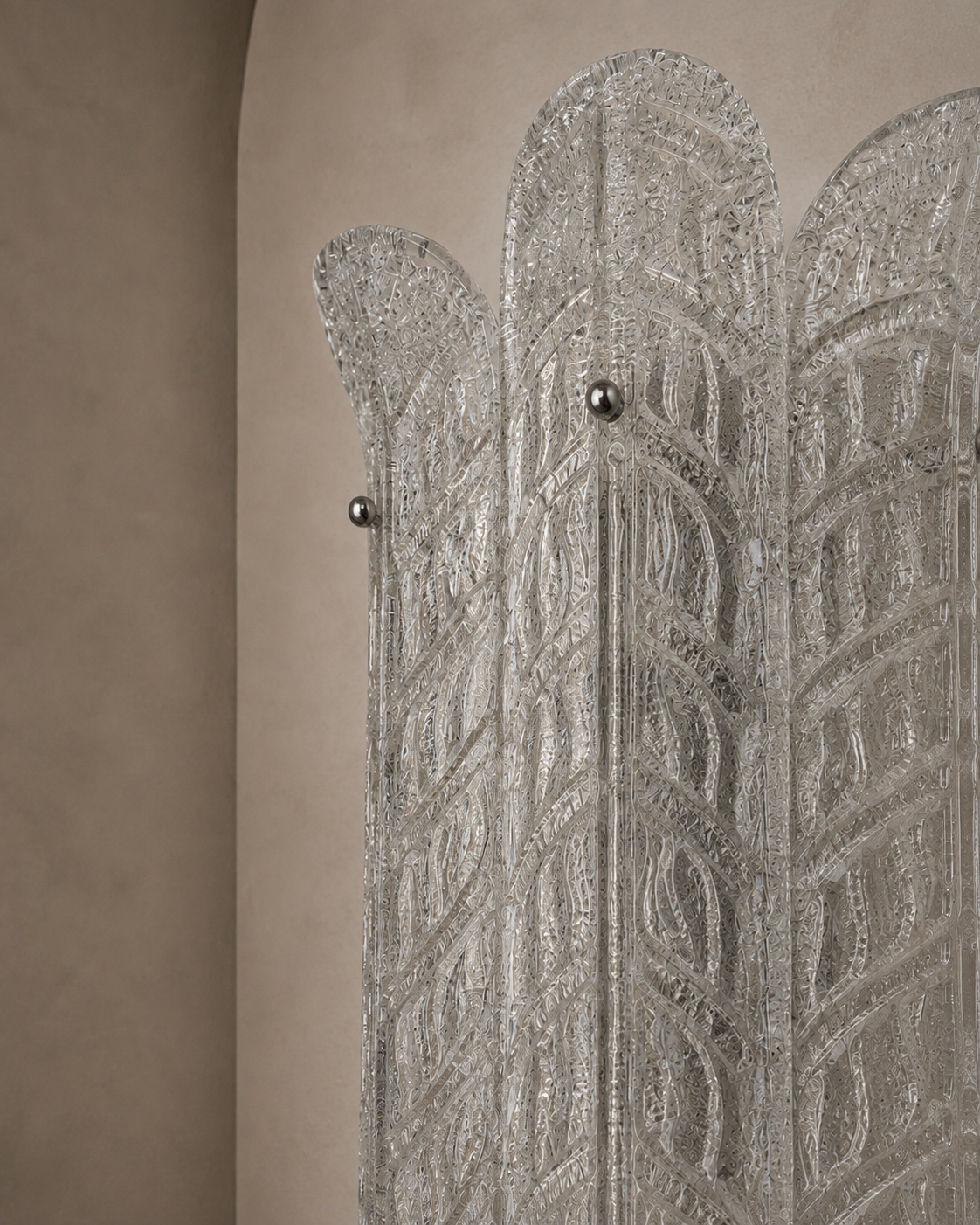 A close-up of a decorative silver-toned screen or divider with an intricate geometric pattern and small metallic knobs, set against a warm beige textured wall.
