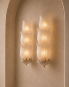 Two matching wall sconces with textured, ribbed glass shades and gold-toned metal accents, mounted on a warm beige stucco wall within an arched recess.