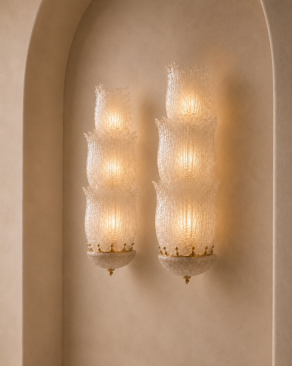 Two matching wall sconces with textured, ribbed glass shades and gold-toned metal accents, mounted on a warm beige stucco wall within an arched recess.
