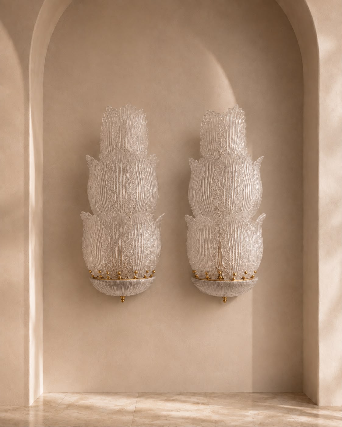 Two matching sculptural wall sconces with layered translucent white textured forms and small gold accents, mounted on a warm beige plaster wall within an arched alcove.