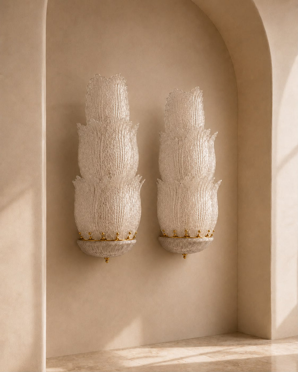 Two matching sculptural wall sconces mounted on a beige plaster archway. The sconces have textured, layered white and cream organic forms with small gold accents at the base.