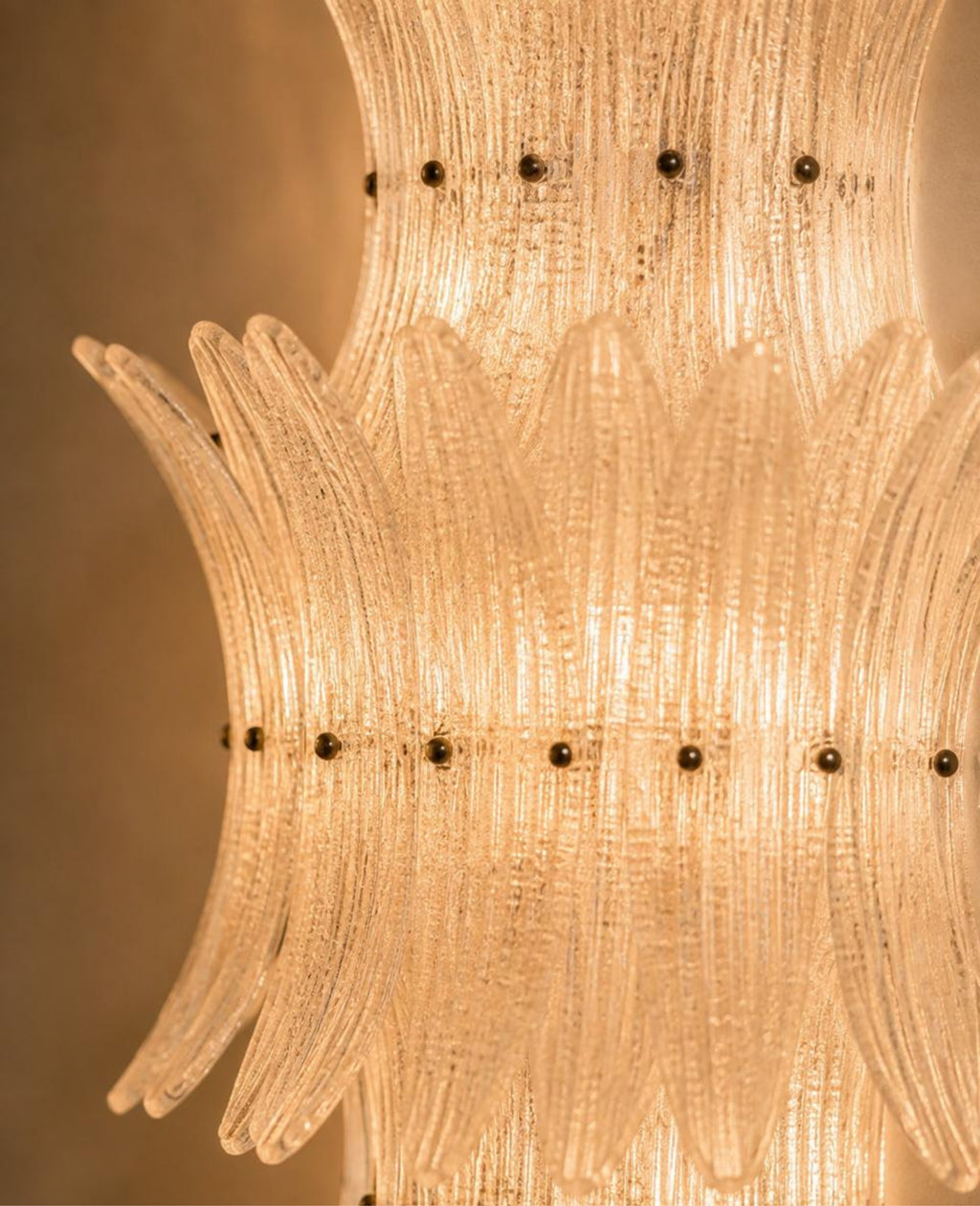 A close-up of a warm glowing Murano-style glass chandelier with layered ribbed glass tubes and small dark metal accents.