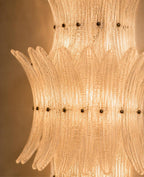 A close-up of a warm glowing Murano-style glass chandelier with layered ribbed glass tubes and small dark metal accents.