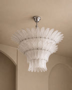 A modern chandelier with a silver ceiling canopy and a tiered, sunburst-style clear glass shade, shown hanging in a beige interior room.