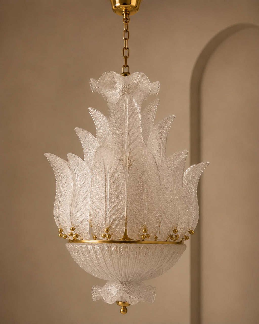 A vintage-style white glass chandelier with a textured, leaf-like fluted design and gold metal accents, suspended from a gold chain against a warm beige wall.