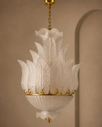 A vintage-style white glass chandelier with a textured, leaf-like fluted design and gold metal accents, suspended from a gold chain against a warm beige wall.