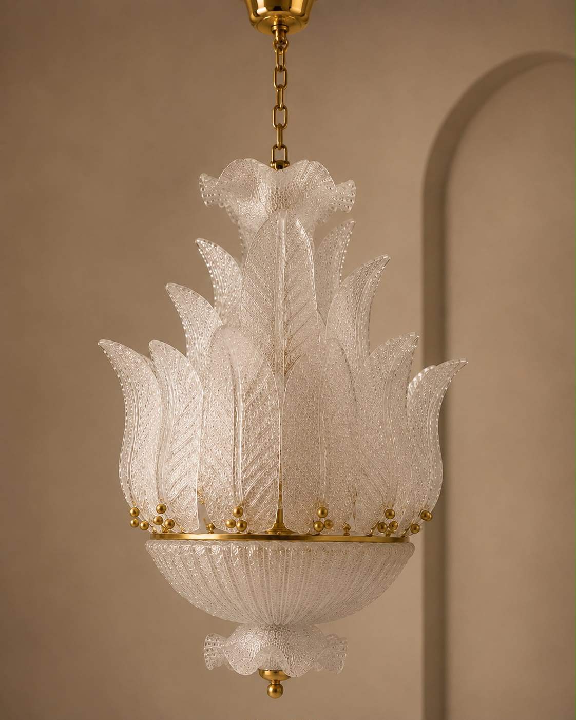 A vintage-style white glass chandelier with a textured, leaf-like fluted design and gold metal accents, suspended from a gold chain against a warm beige wall.